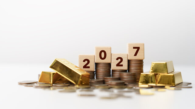 Happy New Year 2027 Concept. Gold bars, stacked coins, and wooden number blocks for wealth, savings, investment, and financial planning for 2027. future growth, money management, and economic goals.