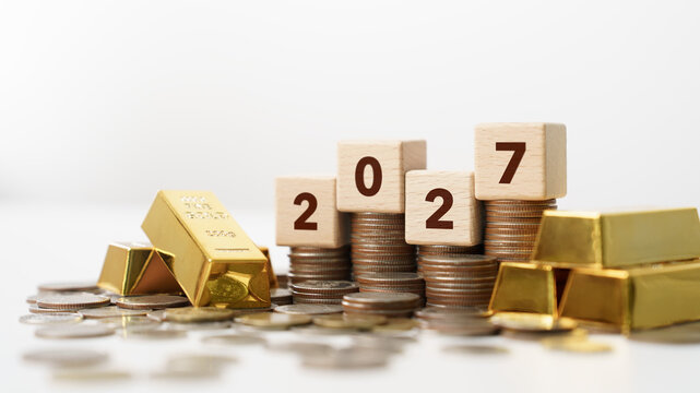Happy New Year 2027 Concept. Gold bars, stacked coins, and wooden number blocks for wealth, savings, investment, and financial planning for 2027. future growth, money management, and economic goals.