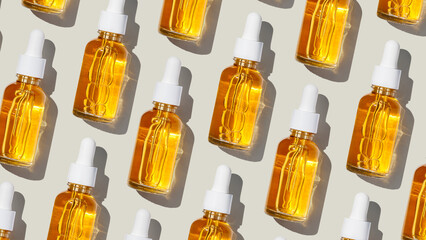 Fototapeta premium Minimal pattern glass dropper bottles filled with yellow golden face serum at sunlight on neutral fon. Minimal cosmetic product for skincare, anti-aging, and beauty concept, repeated layout, top view