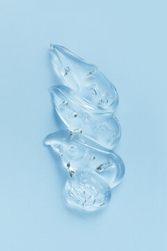 Close up of transparent cosmetic gel swatch with air bubbles on soft blue background. Glossy texture and fluid shape emphasize hydration, moisturizing, purity, and modern skincare aesthetics, top view