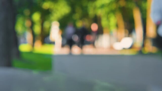 People of various ages are walking along a path in a park, surrounded by trees and greenery. Abstract blurred background of crowd of people.