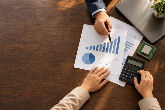 AI generated professionals reviewing charts calculator processor chip closed laptop wooden desk illustrating company financial planning technology budgets copy space