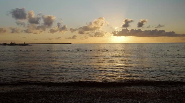 Peaceful summer evening by the sea as the sun sets, painting the sky orange and red and creating beautiful reflections across the calm water.