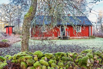 Idyllic red Swedish cottage with moss-covered stone wall in a frosty landscape © Lars Johansson