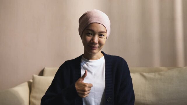 Asian female cancer patient smiling and showing thumbs up gesture. Chemotherapy treatment, healthcare support, positive emotion, and recovery concept.