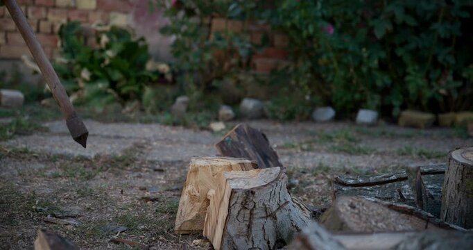 Man chopping firewood with a large axe in a backyard on autumn morning, with only the axe, hands and wooden logs visible. Traditional woodcutting and seasonal household work concept. 4K slow motion.