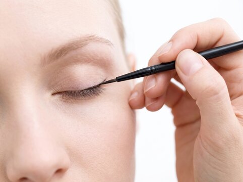 Close up of a young adult woman receiving professional eyeliner application on her eyelid from a makeup artist in a clean studio