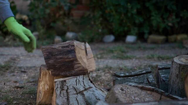 Gloved hands placing a freshly split log on a tree stump for firewood preparation. Autumn backyard setting, woodcutting, manual work, heating and traditional rural lifestyle concept. 4K.