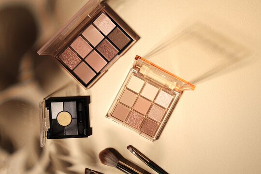 Three open eyeshadow palettes with makeup brushes on a neutral background