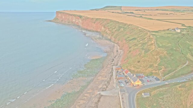 The Ship Inn anchors Old Saltburn below Hunt Cliff, with Jurassic ironstone cliffs, beach, cottages and coastal slopes along the North Sea at Saltburn-by-the-Sea, England, drone pullback.