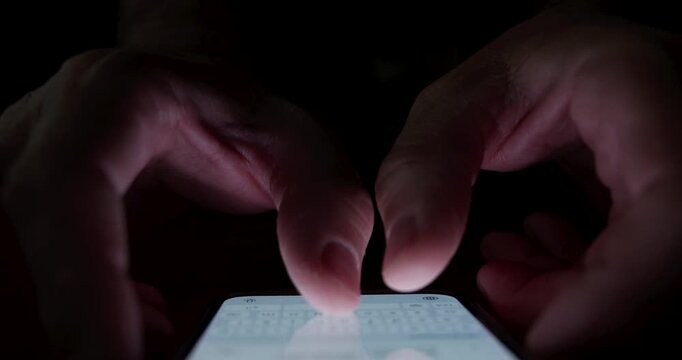 Close-up of hands texting on mobile phone in a dark room. Concept of late-night messaging, smartphone addiction, online chat, and private digital communication. 4K.