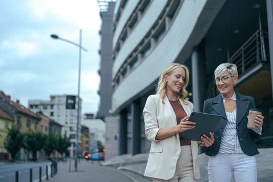 Businesswomen smiling, collaborating and discussing data on a tablet while walking in the city