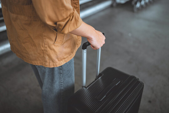 Close up of male traveler holding telescopic handle of black rolling suitcase while standing with luggage, travel preparation, baggage transportation, mobility, tourism and modern journey lifestyle