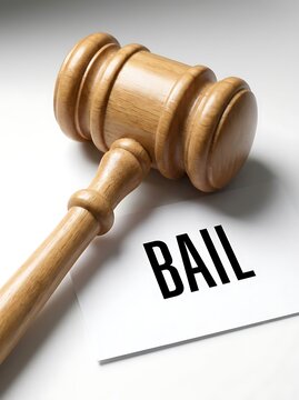 Detailed close view of wooden judge mallet resting over a white card printed with black bail lettering on light background symbolizing judicial system and release.
