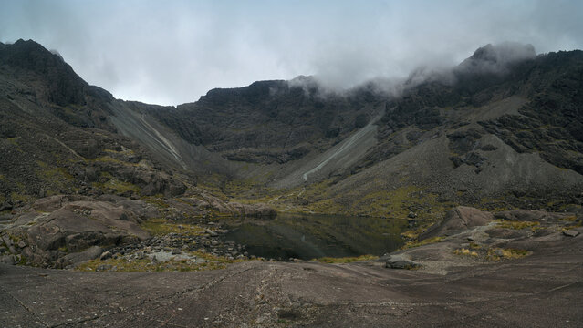 Rocky Coire Lagan landscape beneath mist-covered Cuillin peaks on the Isle of Skye, Scotland, with rugged slopes and mountain terrain. 
