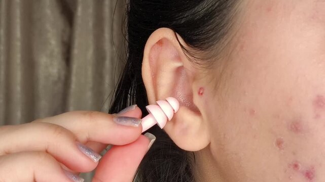 Woman inserting earplugs into her ear to reduce loud noise, illustrating hearing protection, quiet sleep and personal comfort.
