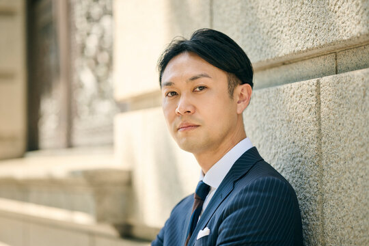 壁にもたれてこちらを見る30代男性ビジネスマン
