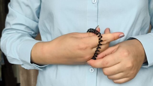 Young woman putting a black spiral hair tie around her wrist, illustrating a practical hair accessory and everyday styling routine.
