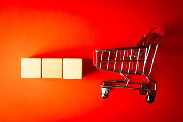 Shopping cart and wooden cubes on a red background. The concept of shopping online. © Artvibe