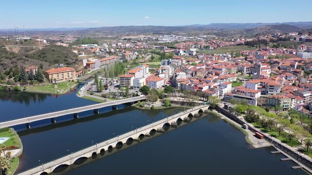 Picturesque aerial view of residential districts of Mirandela city with brownish tiled roofs and two bridges crossing Tua river on spring day, Braganca, Portugal 