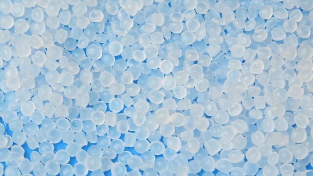 White polymer pellets fall onto rotating granules for packaging, healthcare and plastic processing.