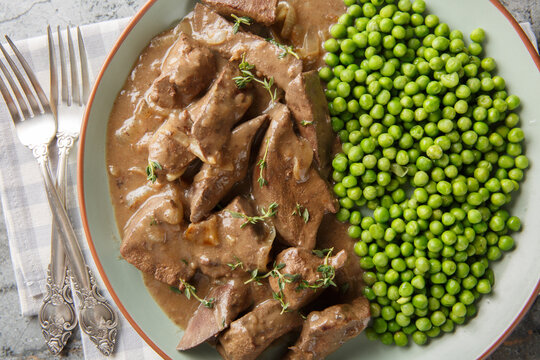 German Liver Baden Style with green peas closeup on the plate on the table. Horizontal top view from above