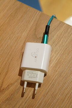 White Arsa Go power adapter with a teal braided charging cable resting on a wooden surface