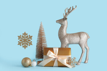 Christmas celebration and holiday shopping, golden gift box with ribbon and silver reindeer ornament on a light blue background © Pixel-Shot