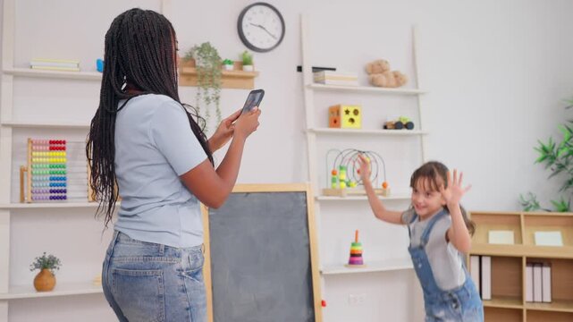 African teacher use phone record young child dancing in learning space. 