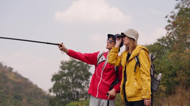Caucasian hikers with backpacks using binoculars on a mountain trail. 