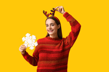Young woman in sweater with Christmas reindeer horns and snowflake on yellow background © Pixel-Shot