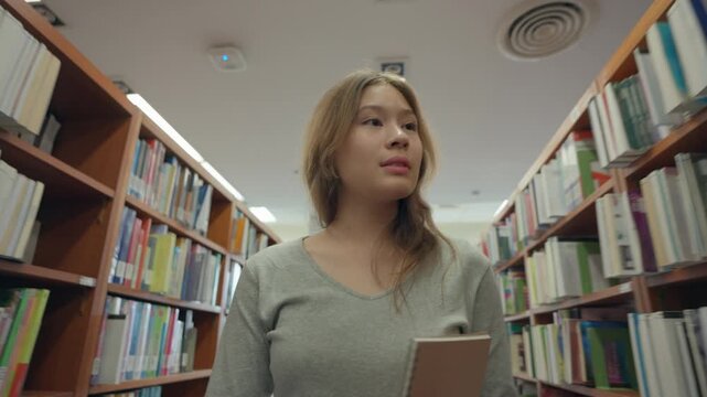 Caucasian young girl holding a book and walking through a quiet library. 