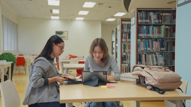 Asian and Caucasian female students study together in university library. 