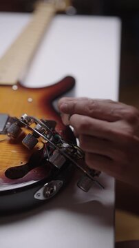 Closeup vertical shot of guitar technician, luthier hands installing new potentiometer. Detailed view of instrument wiring and repair process. Music instrument maintenance, close-up, slow motion.