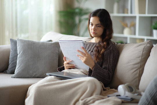 Serious student memorizing notes studying on a sofa in winter