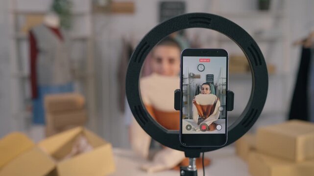 Caucasian woman live streaming and selling clothes in fashion store. 