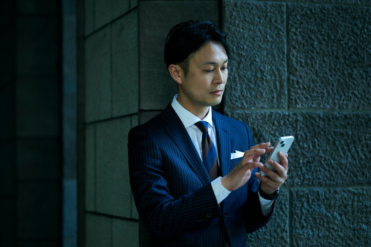 暗がりでスマートフォンを見る男性ビジネスマン