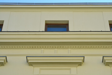 A low angle architectural shot of a yellow historic building facade featuring geometric cornices dentil moldings and a small rectangular upper window. © nahhan