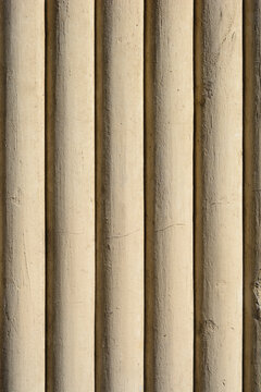 Full frame background texture of a historical stone building facade featuring parallel vertical semi circular fluted columns with fine cracks.