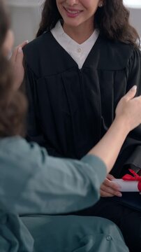Close up of mother and daughter sit on sofa, celebrating college graduation. 