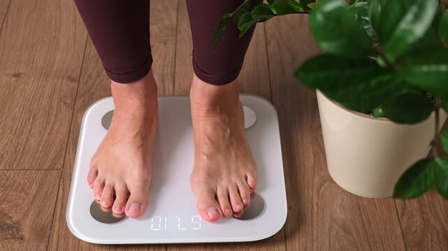 Woman stepping barefoot on digital bathroom scale to measure body weight. Weight loss control and healthy lifestyle concept for diet fitness tracking at home