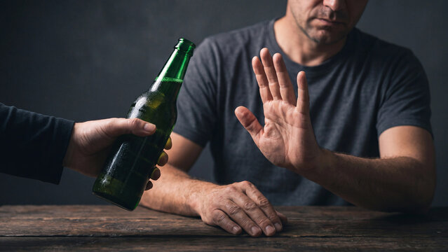 Determined man refuses an offered green bottle of alcoholic beverage, gesturing stop with his hand