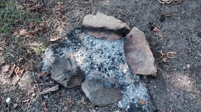 Extinguished campfire ash surrounded by flat stones on ground at campsite