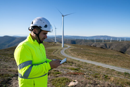 White worker with safety helmet using tablet at wind farm in Galicia