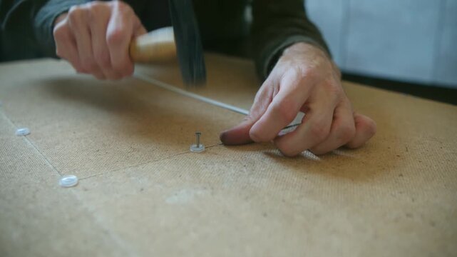Meticulous carpenter carefully hammering small plastic tacks into a wooden board, showcasing precision and craftsmanship in a detailed close up view of the manual labor process