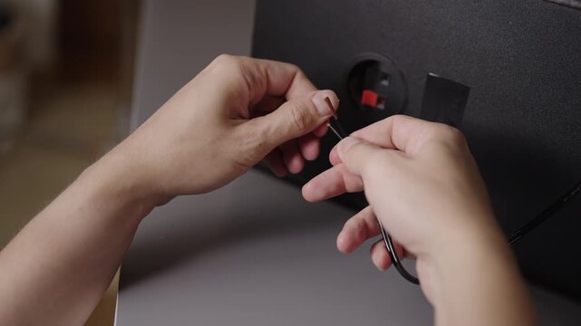 Close-up view of person hands preparing copper speaker wire by twisting strands, getting ready to connect it to terminals on back of audio system, closeup, cropped shot, slow motion.