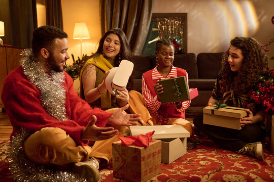 Multiethnic group of young adult friends unpacking Christmas presents including VR headset together indoors. Suitable for holiday tech advertising and seasonal gift campaign