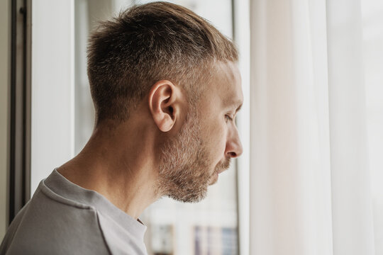 Overthinking keeps man trapped in repetitive thoughts by window, absorbed in rumination, doubt and worry while mentally reviewing unresolved problems in solitude.