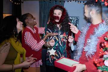 Fototapeta premium Portrait of playful young adult man wearing holiday garland with multiethnic diverse friends celebrating Christmas. Perfect for holiday marketing and party promotion