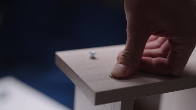 Close-up craftsman hands assembling flat pack furniture. Hands using allen key to tighten screw into light wooden board, completing DIY project. Simple and clean process, closeup, slow motion.
